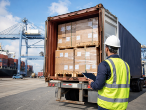 Freight worker inspecting imported palletized cartons inside an open shipping container at a port